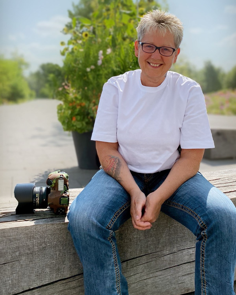 Cornelia Hutzler, Fotografin aus Ebermannstadt, sitzt mit ihrer Kamera auf einer Holzbank im Freien
